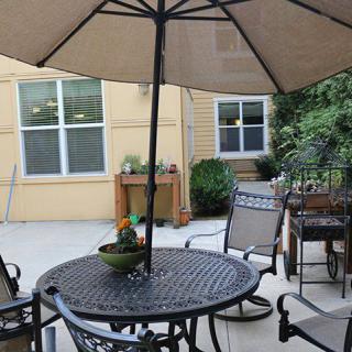 A cozy patio area with a table and chairs under an umbrella, surrounded by plants.