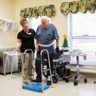 A healthcare professional assists an elderly patient with mobility training using a walker in a rehabilitation setting.