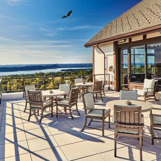 A scenic rooftop patio with tables and chairs overlooking a beautiful lake under a clear blue sky.