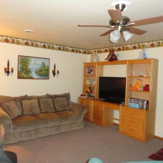 A cozy living room with a large couch, ceiling fan, and an entertainment center housing a television.