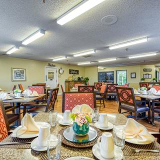A well-arranged dining room featuring tables set with cups, napkins, and a central floral arrangement.
