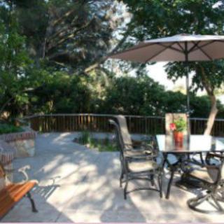 A sunny patio with a table, chairs, and an umbrella surrounded by lush garden greenery.