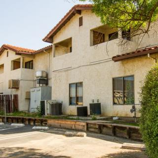 A sunny exterior view of a residential apartment building with trees and air conditioning units.