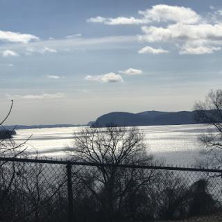 A serene view of the water reflecting the clouds and distant hills.