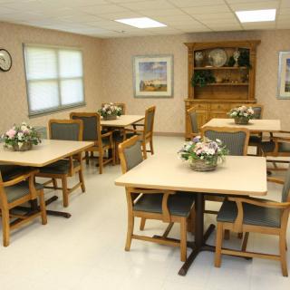 A neatly arranged dining room with wooden tables and chairs, decorated with flower arrangements.