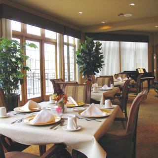 An elegant dining area with neatly arranged tables and chairs, featuring decorative plants and large windows.