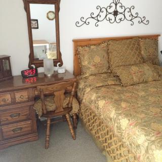 A cozy bedroom with wooden furniture, including a bed with patterned bedding and a dresser with a mirror.