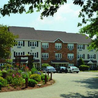 A three-story building with a parking lot surrounded by trees and landscaped gardens.
