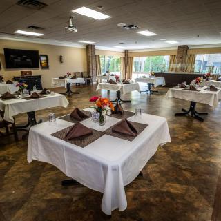 A spacious dining room with neatly arranged tables covered in white tablecloths and adorned with flowers.