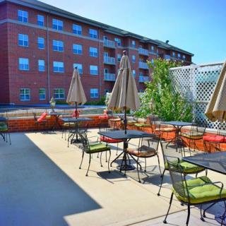An outdoor patio with tables, chairs, and umbrellas in front of a brick building.