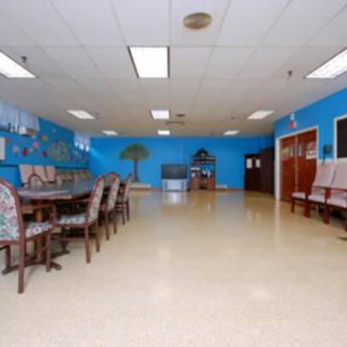A spacious room with blue walls, featuring chairs and tables arranged neatly, and lit by overhead ceiling lights.