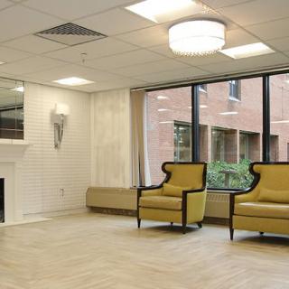 A spacious waiting room with modern decor, featuring two yellow chairs, large windows, and a fireplace.