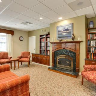 A cozy living room featuring a fireplace, surrounded by bookshelves and comfortable chairs.