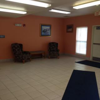 A simple lobby with orange walls, tile flooring, and two armchairs.