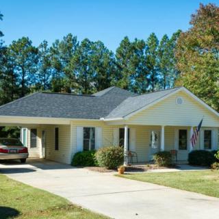 A suburban house with a carport, surrounded by trees on a sunny day.