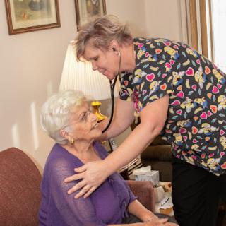 A nurse conducts a medical examination of an elderly woman at home, using a stethoscope to check her health.