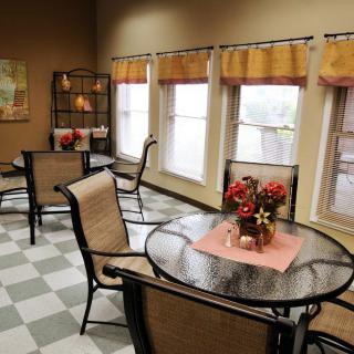 A cozy indoor dining area with tables and chairs, featuring decorative plants and large windows.