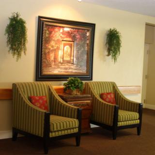 A cozy lobby area with two striped armchairs, a decorative painting, and potted plants.