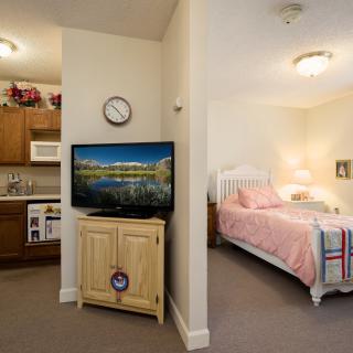 A cozy interior featuring a small kitchen, living area with a TV, and an adjoining bedroom.