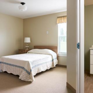 A simple and clean bedroom with a bed, lamp, and window.