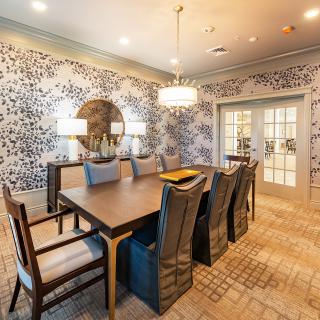 A stylish dining room with a large wooden table, comfortable chairs, patterned wallpaper, and elegant lighting.