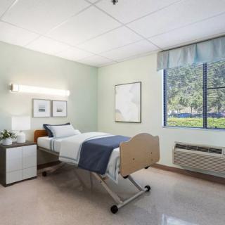 A clean and well-lit hospital room with a single bed near a window.