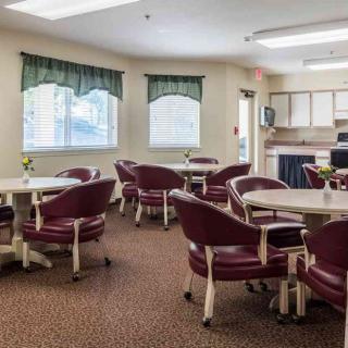 A cozy dining area with several round tables and cushioned chairs arranged neatly, under soft lighting and near large windows.