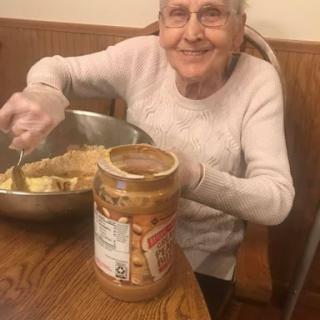 An elderly woman joyfully preparing a recipe in the kitchen with peanut butter.