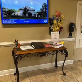 A reception area with a decorative table featuring sign-in materials and a television mounted on the wall above.