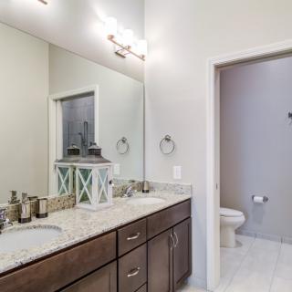 Modern bathroom with a large mirror, vanity, and adjacent toilet area.