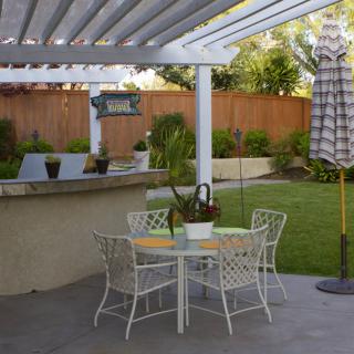 A cozy backyard patio with a pergola, featuring outdoor seating and a garden view.