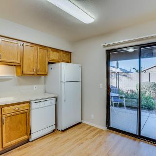 A well-lit kitchen with wooden cabinets and modern appliances, including a refrigerator and dishwasher, opens to an outdoor view through sliding glass doors.