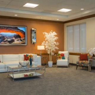A modern living room with a white sofa, glass coffee table, and vibrant artwork on the wall.
