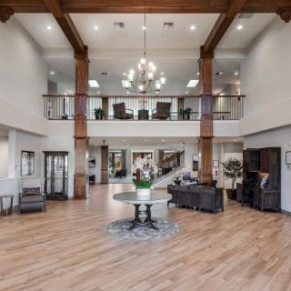 A spacious and elegantly designed lobby with a high ceiling, featuring a central chandelier, wood flooring, and modern furniture.