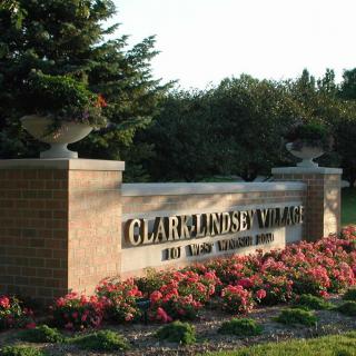 Entrance sign to Clares Garden Village surrounded by vibrant flowers and greenery.