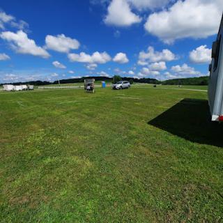 A sunny day in an open field with vehicles parked on the grass under a blue sky dotted with clouds.