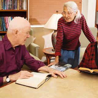 A group of elderly people engaged in a discussion in a library setting.