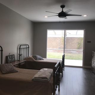 A minimalist bedroom with twin beds and large windows overlooking a backyard.