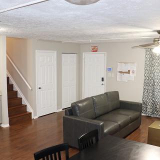 A modern living room with a gray sofa, wooden flooring, and visible staircase.