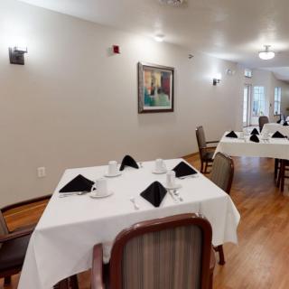 A cozy dining area with neatly arranged tables and chairs, featuring elegant table settings and a wall painting.