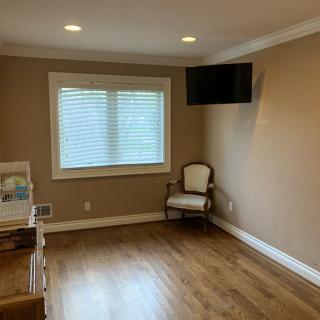 A minimalist room with wooden flooring, a window with blinds, a chair in the corner, and a TV mounted on the wall.