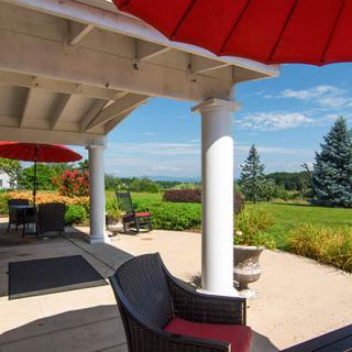 A charming patio with red umbrellas offers a scenic view of a landscaped garden and distant trees on a sunny day.