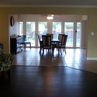 A view of a dining room with a table and chairs, large windows, and tiled flooring.