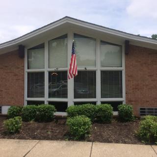 A brick building with large windows and an American flag displayed above neatly trimmed bushes.