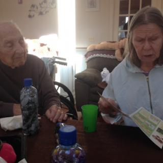 Two elderly individuals engaged in conversation at a table, surrounded by food and drinks.