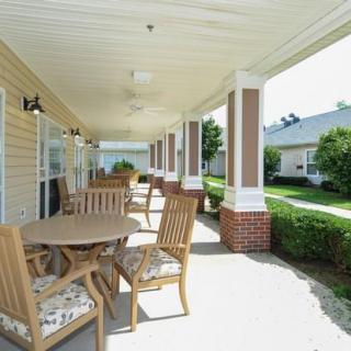 A sunny covered porch featuring outdoor seating with wooden chairs and a table.