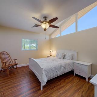 A cozy bedroom with a white bed, wooden flooring, and a ceiling fan.