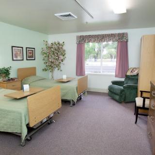 A well-lit hospital room with two beds, a window with curtains, and comfortable furniture.