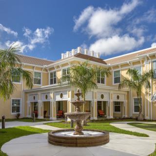 A beautiful building with palm trees and a central fountain under a partly cloudy sky.