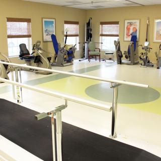 A rehabilitation room equipped with exercise machines and parallel bars for physical therapy.